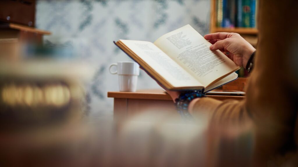 pessoa lendo livro com xícara ao lado apoiada em uma mesa