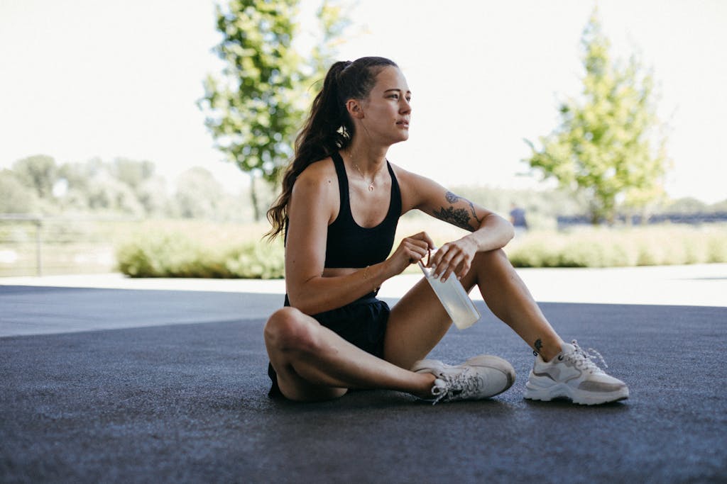 Uma jovem descansando ao ar livre com uma garrafa de água, fazendo uma pausa após o exercício.